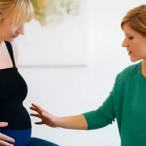 Hebamme untersucht Babybauch einer schwangeren Frau bei Schwangerschaftsvorsorge