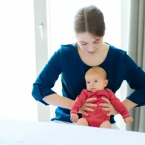 Mutter hält Baby auf dem Schoß im hellen Schlafzimmer, Neugeborenes Pflege