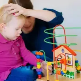 Kleinkind spielt mit Motorikschleife aus Holz im Montessori-Spielzimmer
