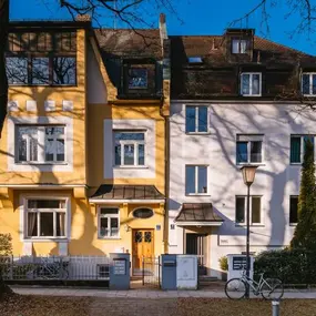 Altbau-Mehrfamilienhaus mit gelber und weißer Fassade, Bäume, Fahrrad vorne