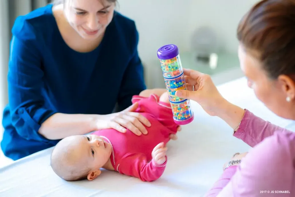Physiotherapie mit Baby: Therapeutin zeigt Rassel zur Frühförderung