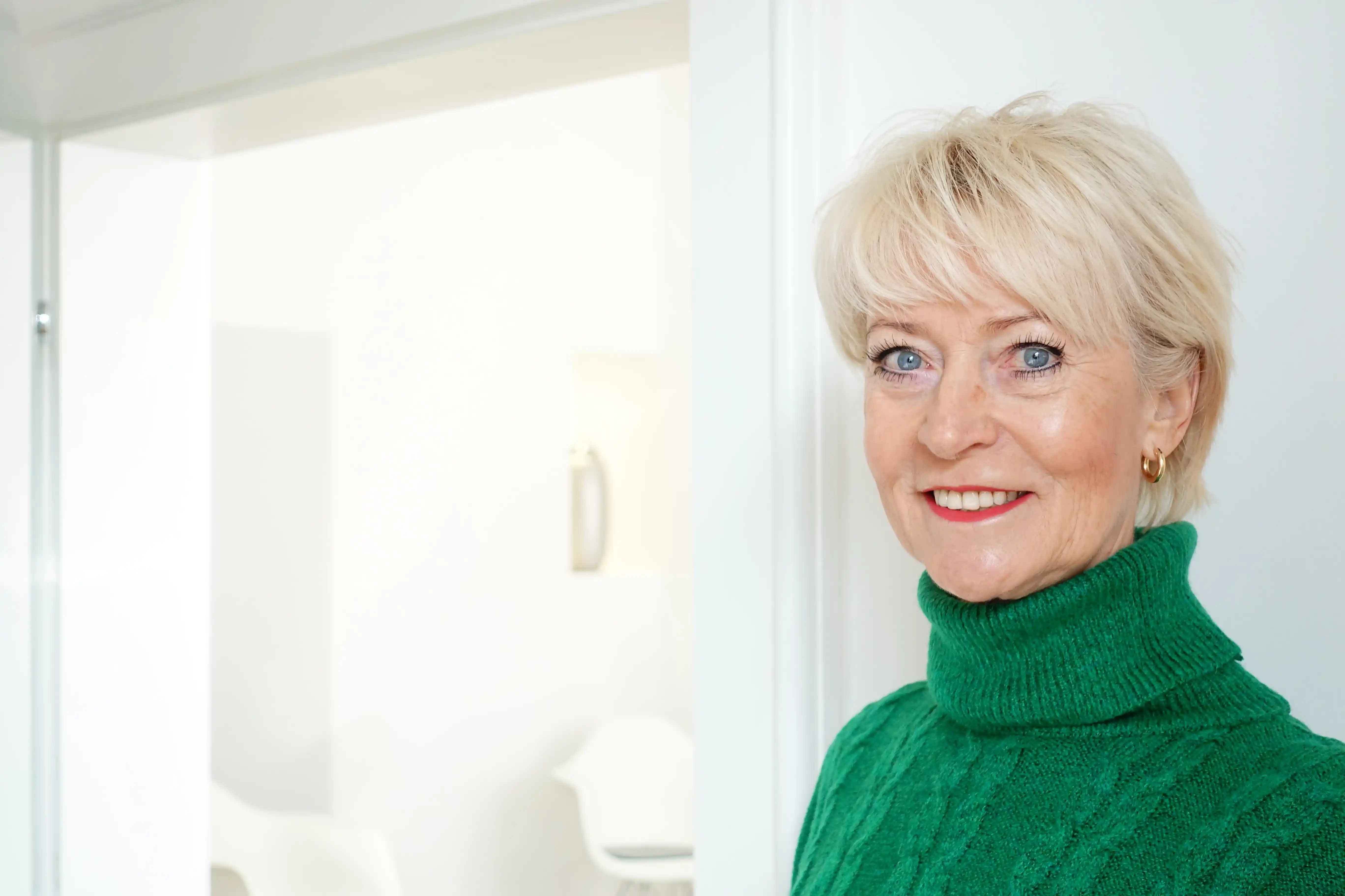 Porträt einer lächelnden Seniorin im grünen Pullover in heller Wohnung